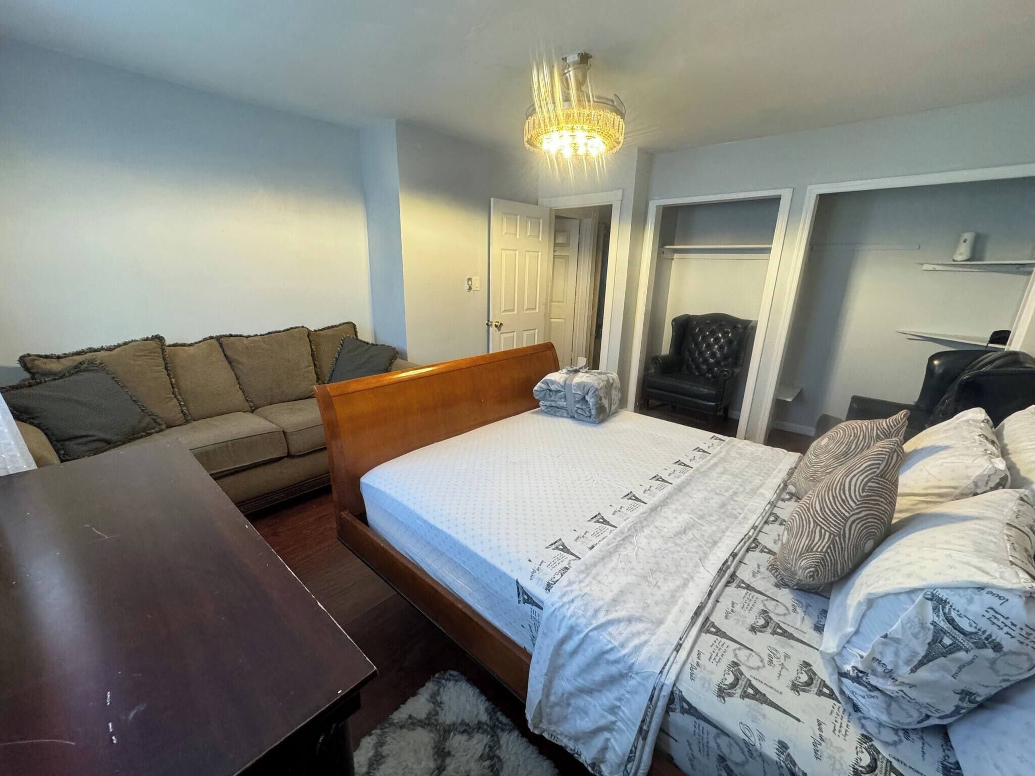 Un dormitorio con cama, mesita de noche de madera, sofá, sillón y escritorio.