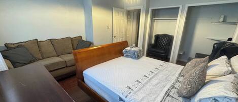 Un dormitorio con cama, mesita de noche de madera, sofá, sillón y escritorio.