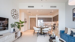 Una sala de estar moderna con comedor, una cocina y un televisor sobre un mueble.