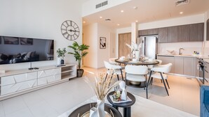 Una sala de estar moderna con un televisor de pantalla plana, un comedor con sillas blancas y una cocina con armarios de madera.
