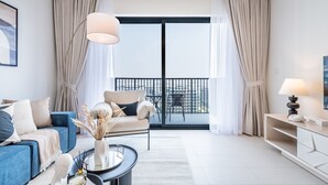Una sala de estar moderna con un sofá, un sillón, una mesa de centro, un balcón con vistas y un televisor sobre un mueble.