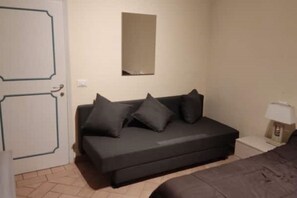 A small, modern bedroom with a dark-colored sofa, a bedside table with a lamp, and a door with a geometric design. - Centralissimo: Comodo per 3, Economico per 6 :-) (Firenze)