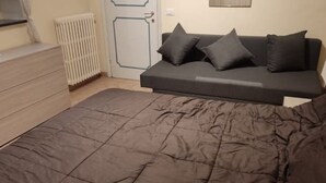 Et soveværelse med en seng, et kommode, en radiator og en mørk sofa op ad væggen.