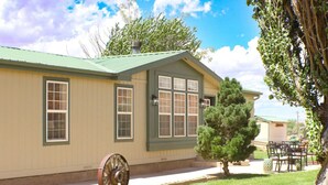 A single-story building with a green roof and beige walls, a large wheel in the foreground, and a small tree in the yard. - Trail Chaser Moab, UT (Moab)