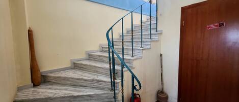 A marble staircase with a blue handrail, a red fire extinguisher, and a wooden door with a sign.