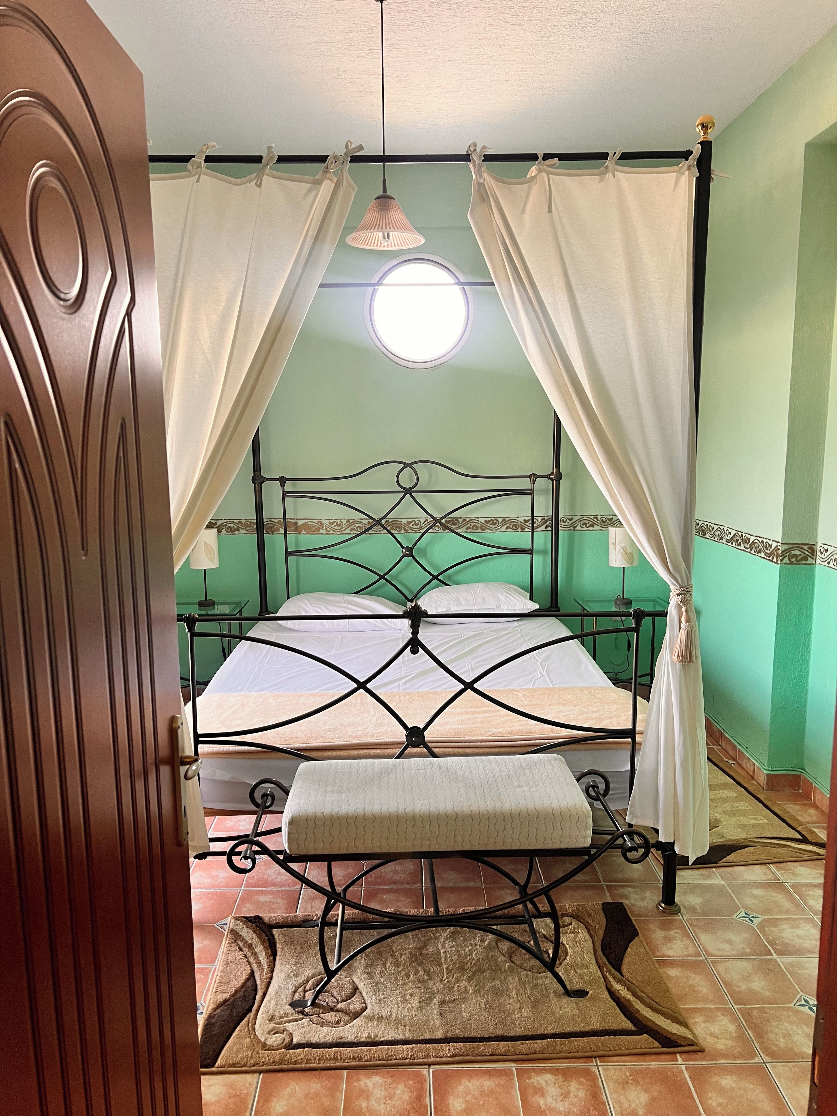 Una habitación con cama, cortinas, una lámpara colgante y una pequeña mesa.