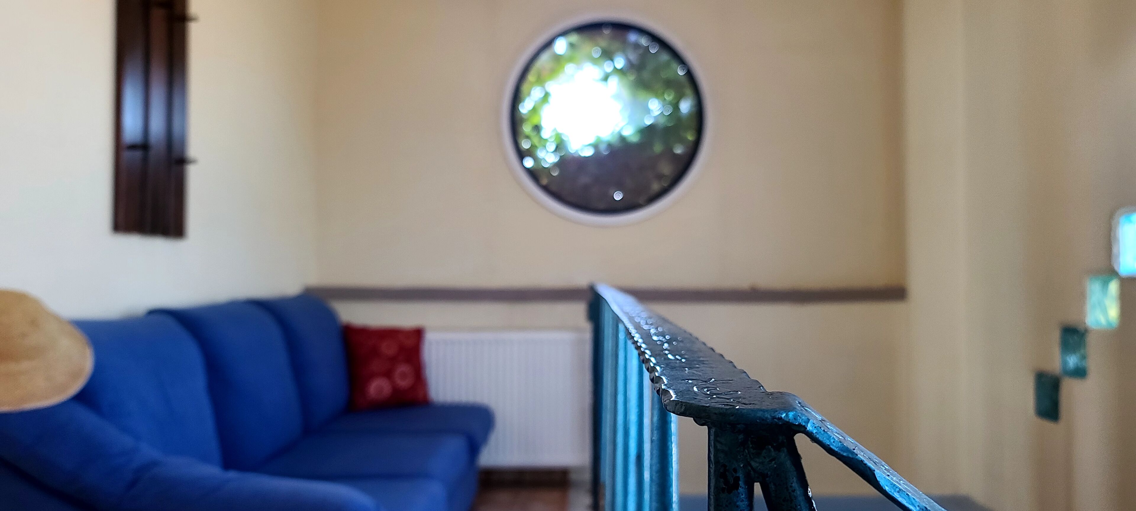Una habitación con un sofá azul, un ventanal redondo y una barandilla de metal.