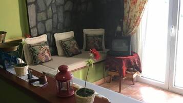 Ein gemütlicher Wohnbereich mit Steinwand, einer Couch mit floralen Kissen, einem kleinen Tisch mit Laterne und einem Fernseher.
