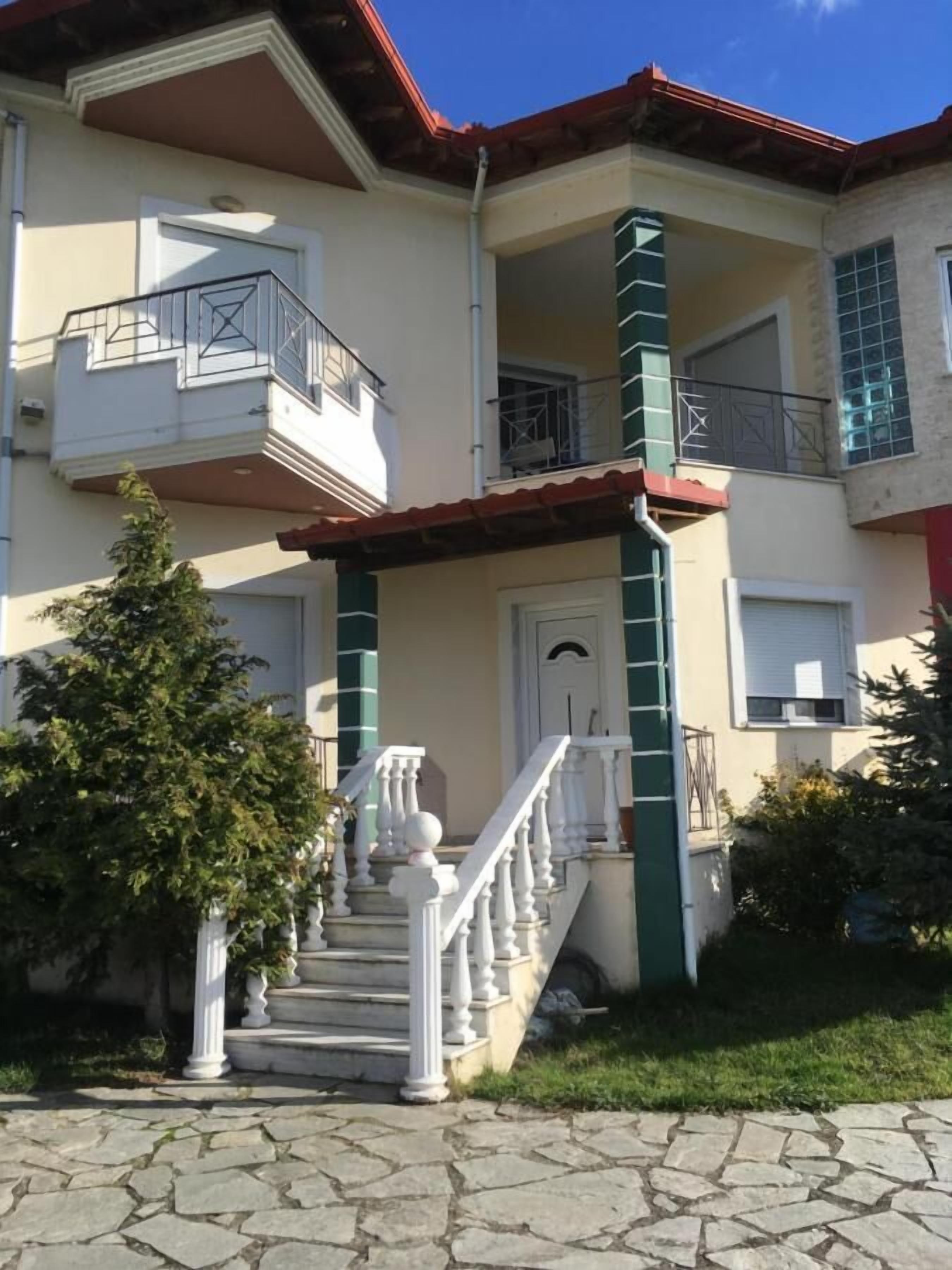 Un edificio de dos plantas con una escalera central, un balcón en el piso superior y una pequeña área ajardinada.