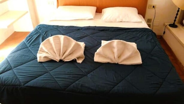 A bed with a dark blue quilt, two folded white towels, and an orange headboard.