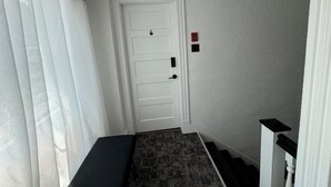 A narrow hallway with a white door, a patterned carpet, and a black bench.