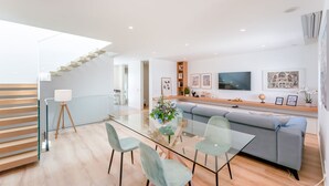 Una sala de estar moderna con una mesa de comedor de vidrio, dos sillas, un sofá y una escalera.
