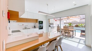 Una cocina moderna con armarios blancos, encimera de madera y zona de comedor con mesa y sillas de vidrio.