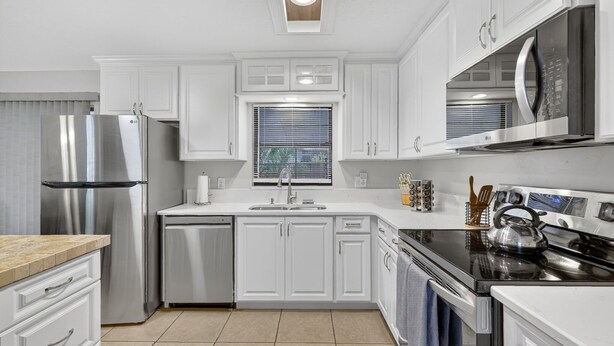 A modern kitchen with white cabinetry, stainless steel appliances, a built-in oven, and a window with blinds. - Cozy Stay in Ocala 3 Bedroom House, King Bed, Fenced, Peaceful & Pet Friendly  (Ocala)