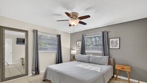 A bedroom with a bed, a ceiling fan, a nightstand, a mirror, and a window with curtains. - Cozy Stay in Ocala 3 Bedroom House, King Bed, Fenced, Peaceful & Pet Friendly  (Ocala)