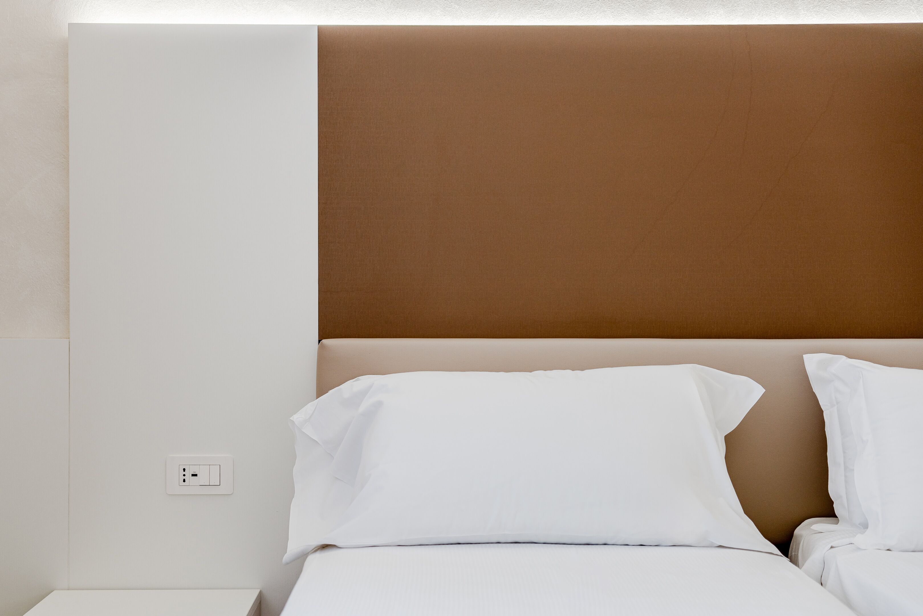 A hotel room with a bed, white bedding, a brown headboard, and a white nightstand.