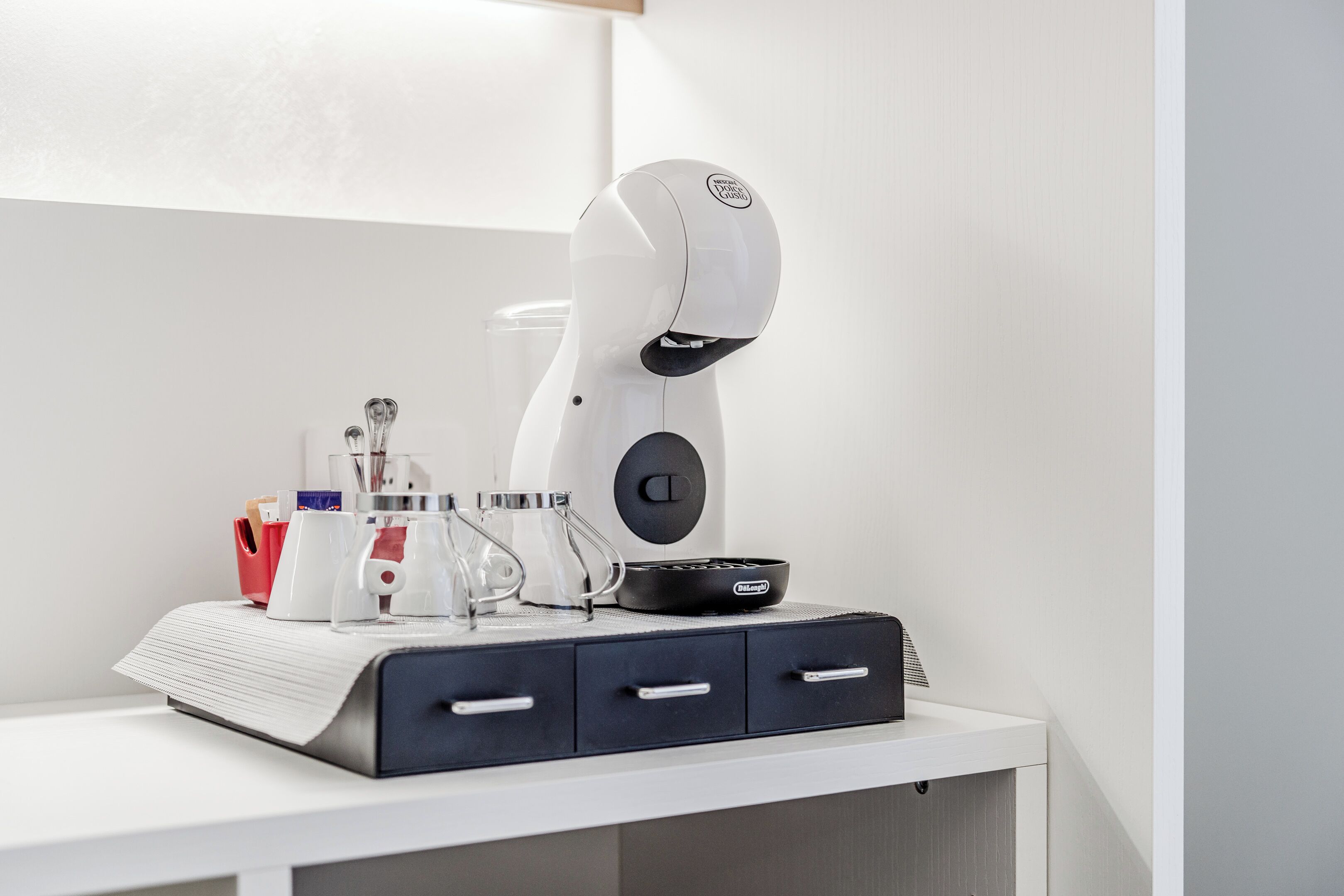 A robotic arm on a white desk with drawers, a coffee machine, and a glass container.
