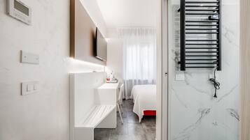 Camera d'albergo moderna con un letto, una scrivania, una televisione e un bagno dotato di doccia e portasciugamani.