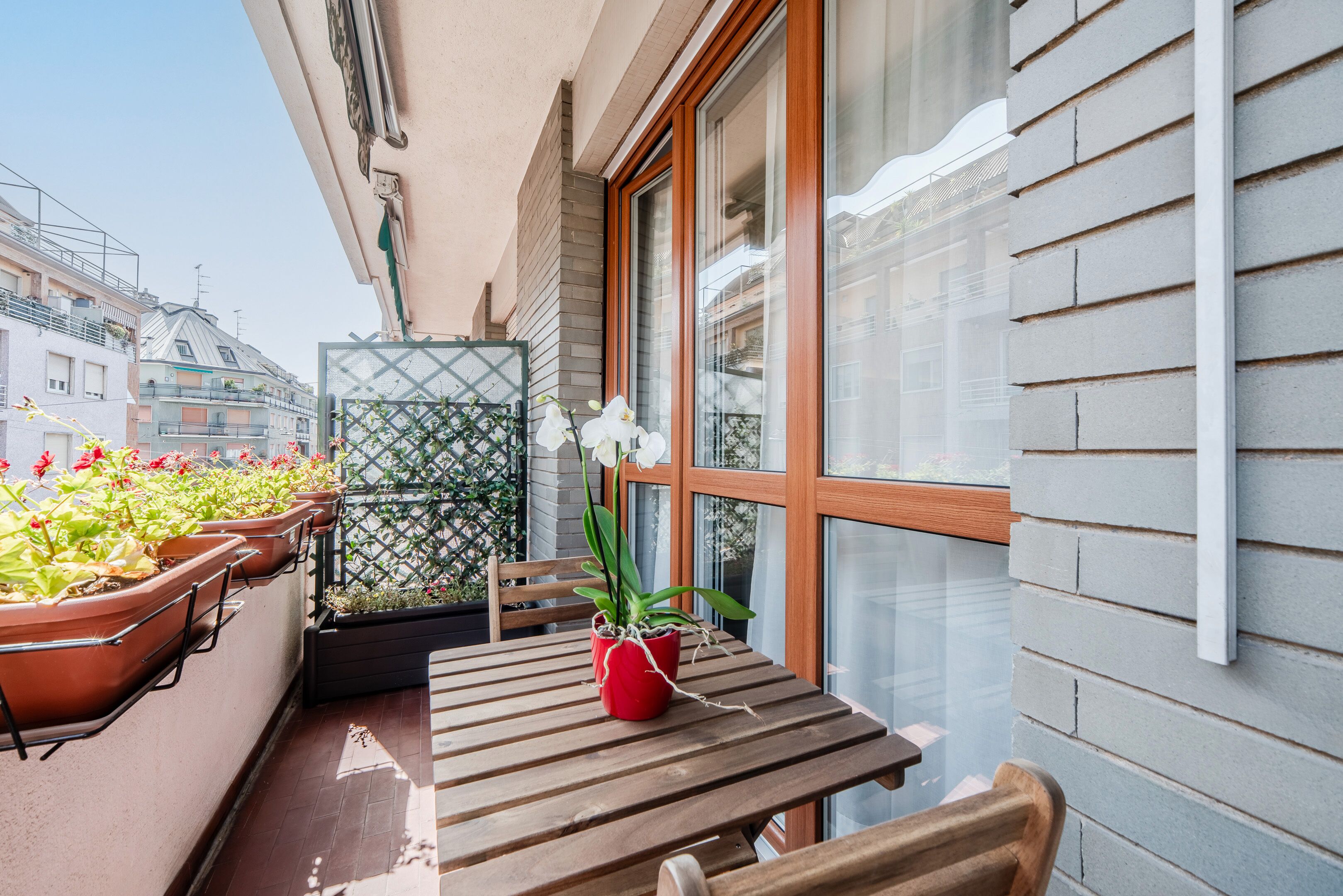Un balcon avec une table et des chaises en bois, des plantes en pot et une vue sur le paysage urbain.
