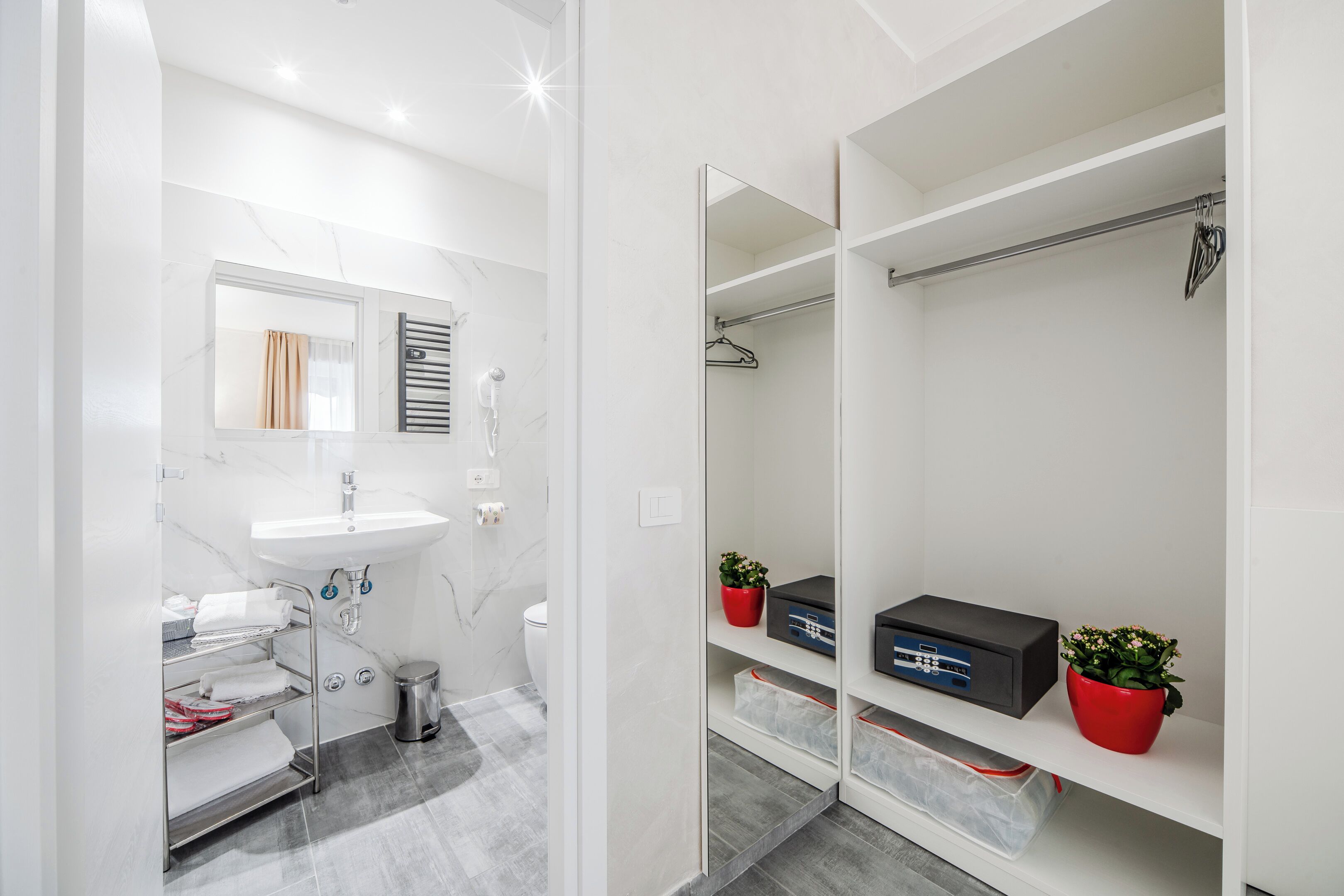 Un bagno moderno con lavandino bianco, specchio e cabina doccia. Sono presenti mensole contenitive con una pianta rossa e una scatola nera.