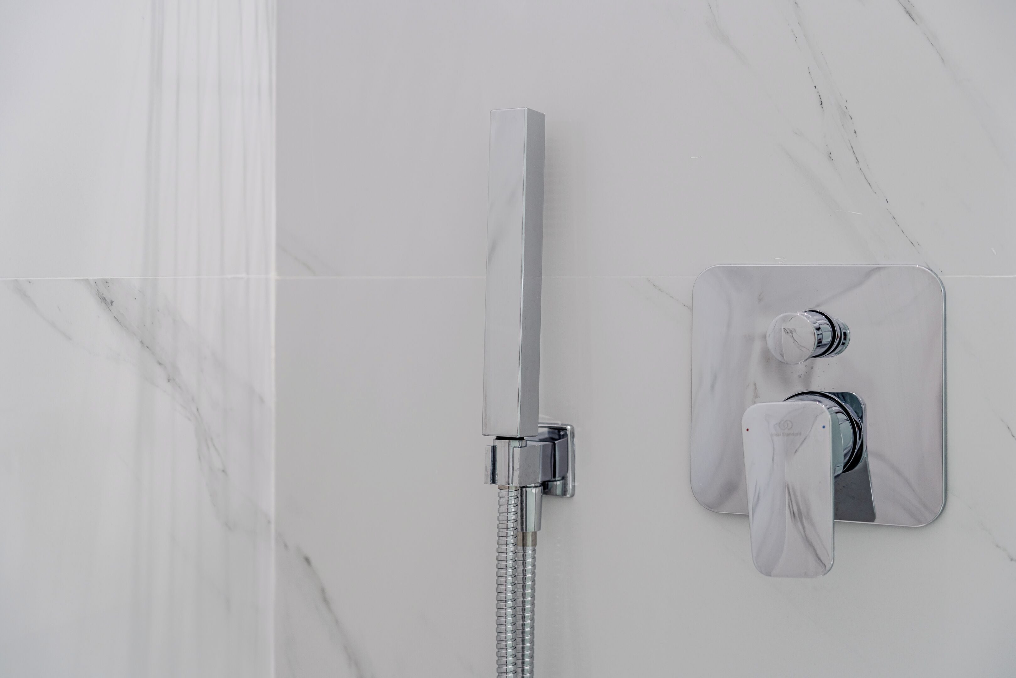 A modern bathroom with a glass-enclosed shower, a wall-mounted control panel, and a marble floor.