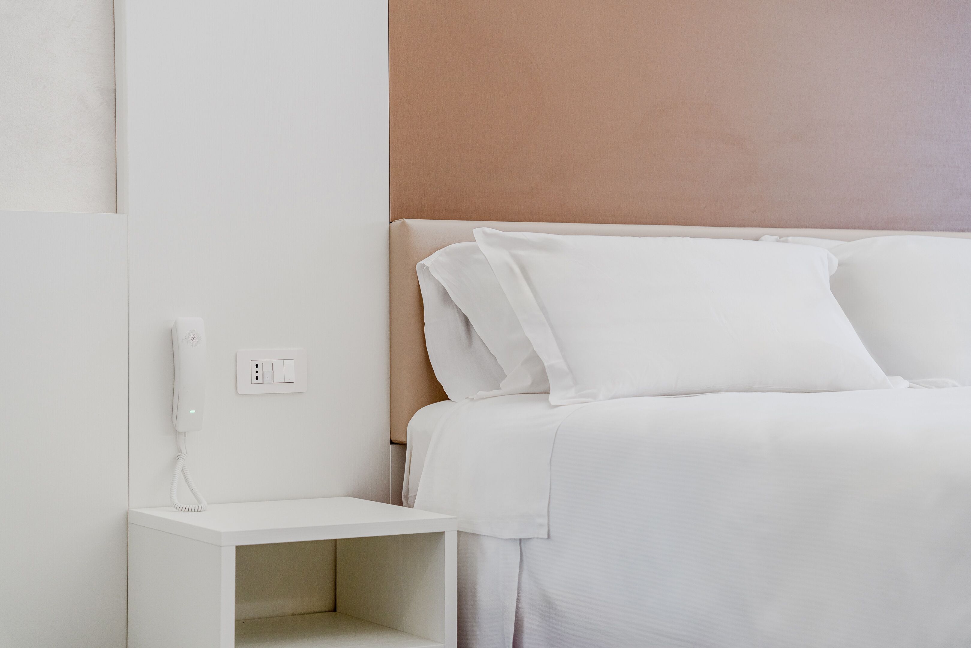 A neatly arranged hotel room with a bed, a bedside table, and a wall socket.