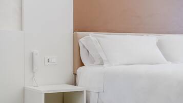 A neatly arranged hotel room with a bed, a bedside table, and a wall socket.