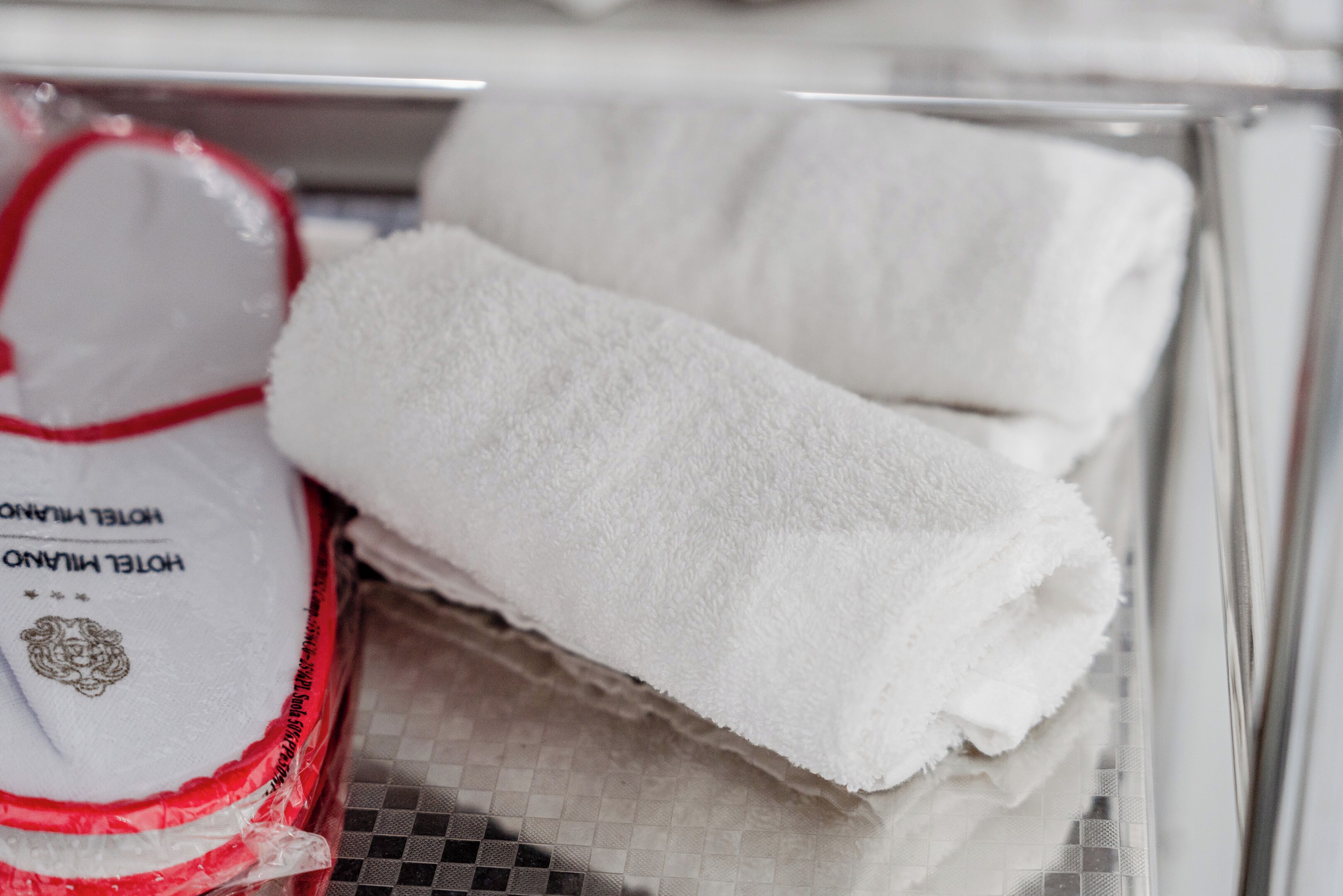 Une pile de serviettes blanches dans un récipient en verre, avec un emballage de serviettes d’hôtel rouge et blanc partiellement visible.