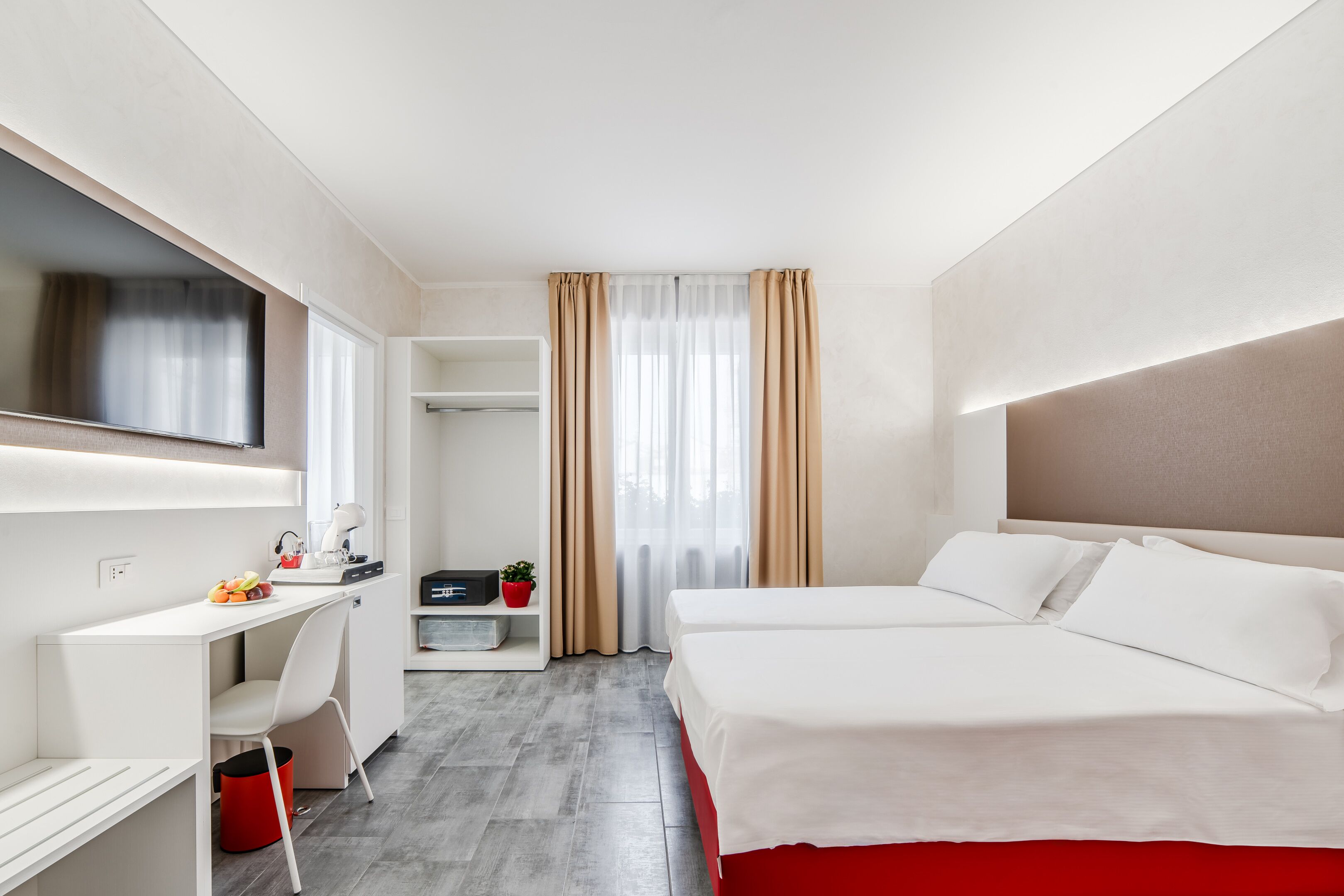 Quarto de hotel com cama, escrivaninha, cadeira, televisão e janela com cortinas.
