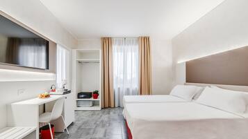 Quarto de hotel com cama, escrivaninha, cadeira, televisão e janela com cortinas.