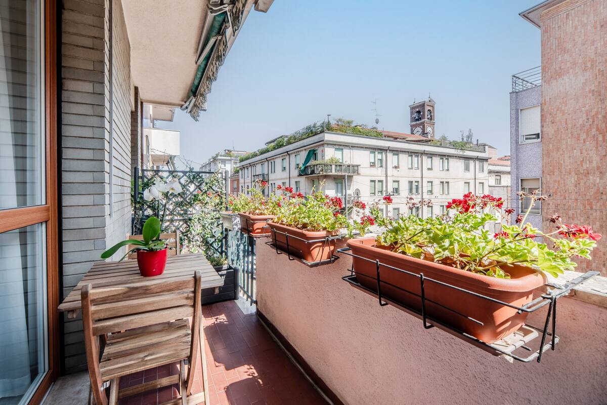 A balcony with wooden furniture and terracotta planters with flowers.