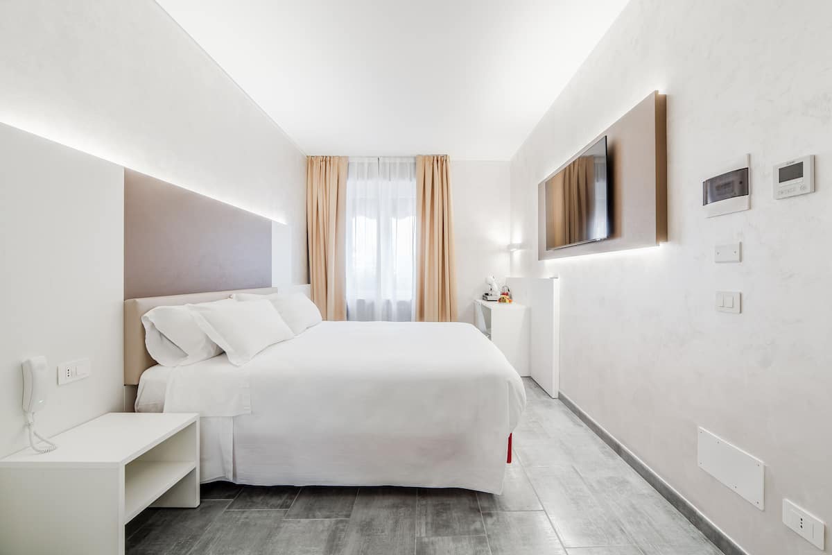A modern hotel room with a large bed, bedside table, and a TV mounted on the wall.