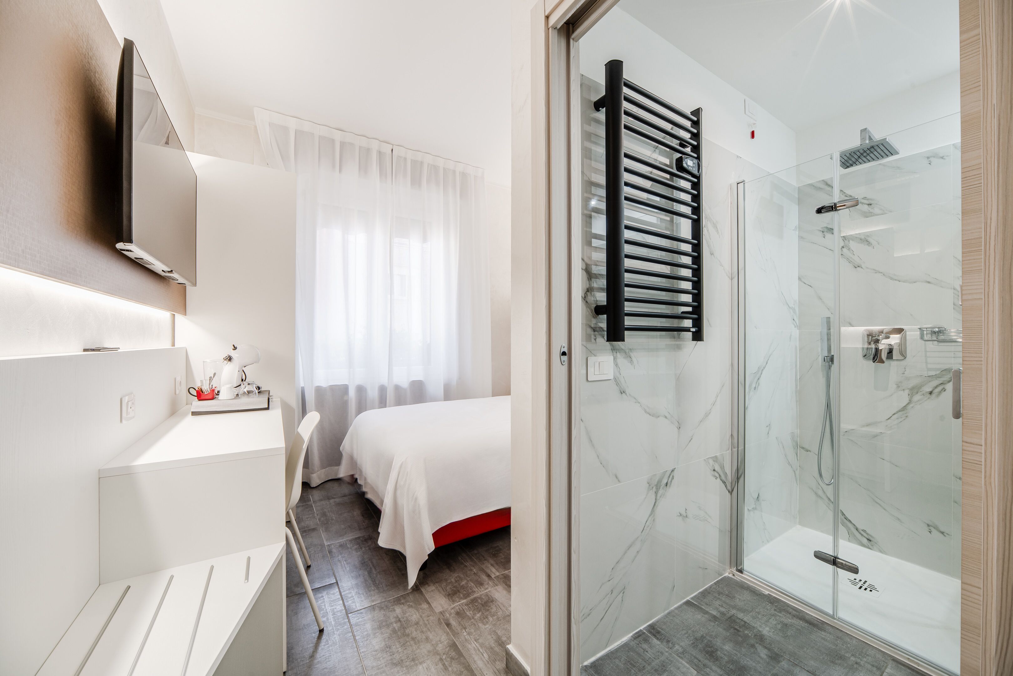 A modern bathroom with a glass shower, a white sink, and a bed with a white headboard.