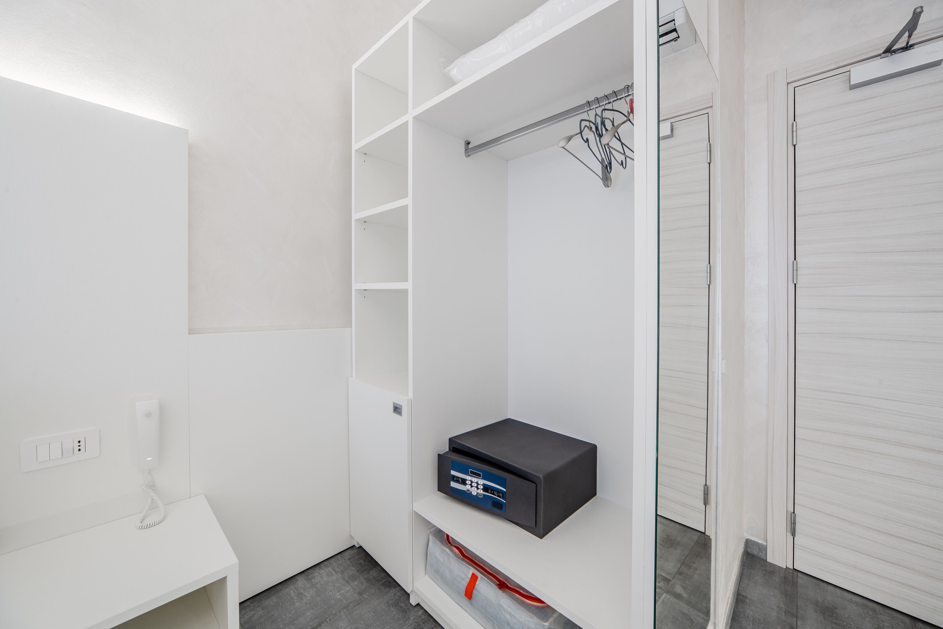 Een moderne, witte kast met een ingebouwde verwarming, een kledingroede en een klein plankje met een apparaat.