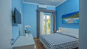 A bedroom with a bed, a TV, a window with curtains, and a painting of a beach scene. - B&B Carmelina (Gragnano)