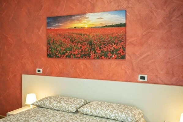 A bedroom with a bed, two bedside lamps, and a painting of a field of flowers on the wall. - B&B Carmelina (Gragnano)
