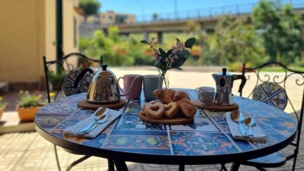 A round table with a blue patterned tablecloth, a croissant, a coffee pot, and a teapot on it. - B&B Carmelina (Gragnano)