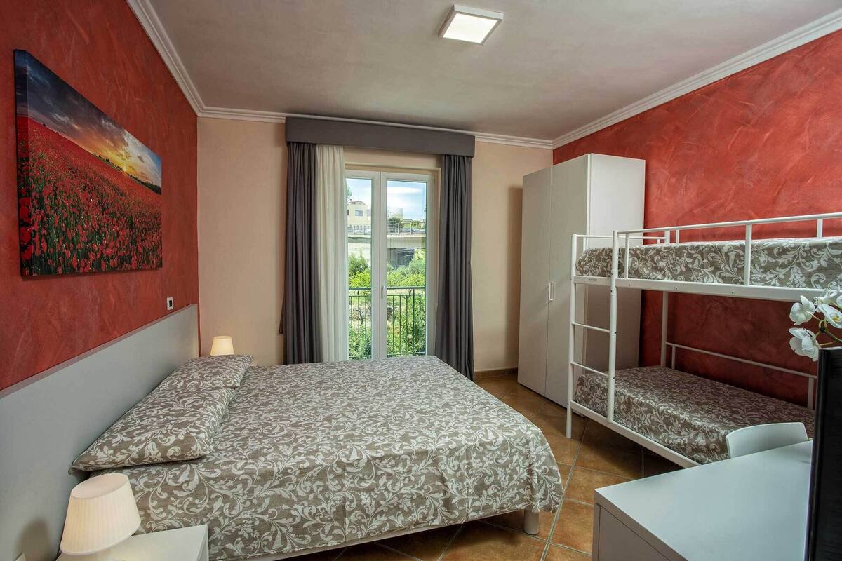 A bedroom with a bed, a desk, a bunk bed, a wardrobe, and a painting on the wall.