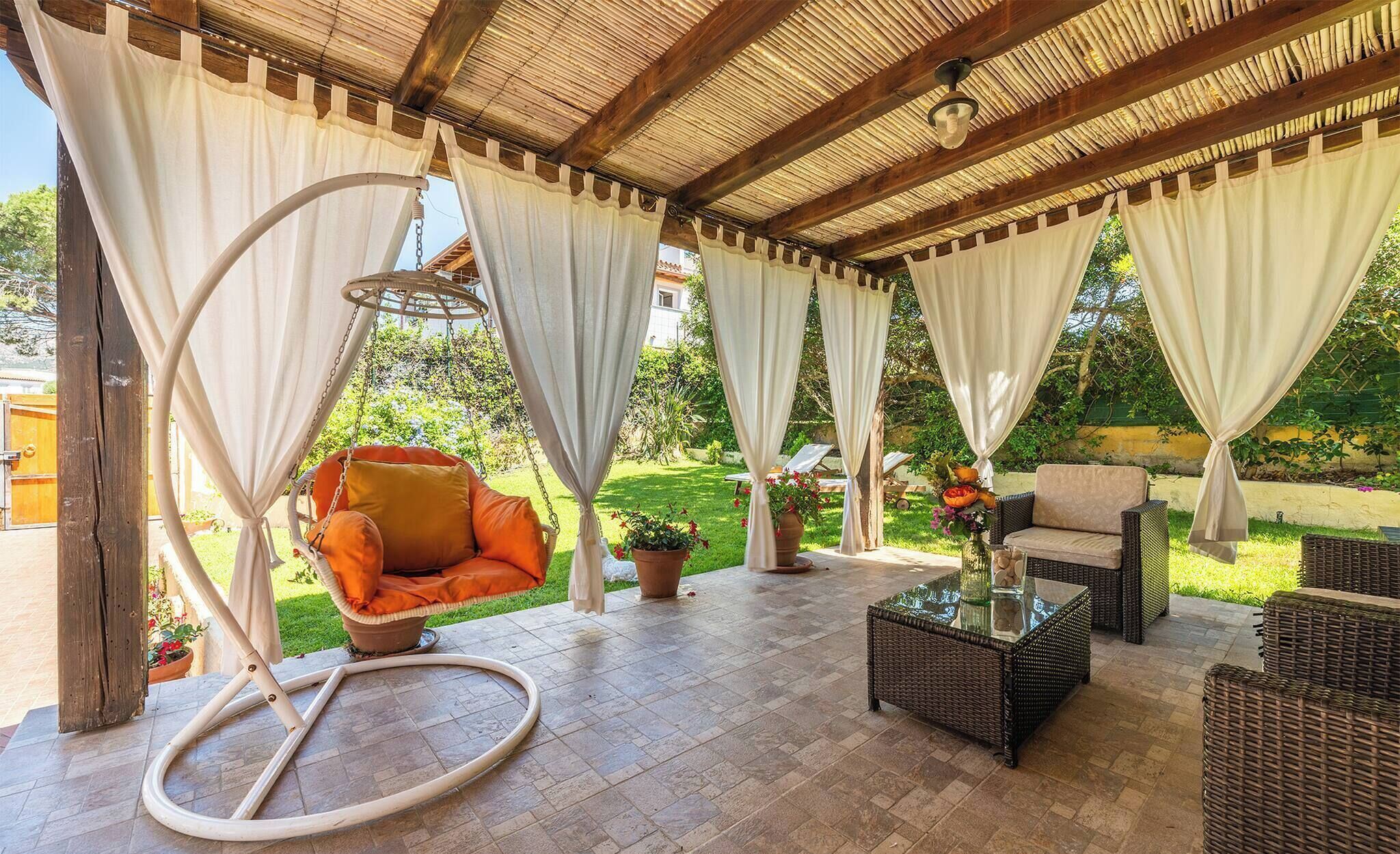 A covered outdoor seating area with wicker furniture, a hanging chair, and a glass table.