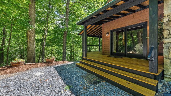 A wooden cabin with a deck, surrounded by trees and a gravel path. - A peaceful retreat with a melody all it's own...come experience Maggie's Song! (Maggie Valley)