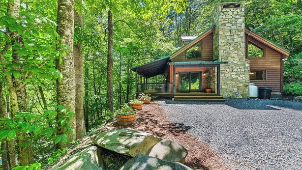 A cabin with a stone chimney, wooden exterior, and a porch with potted plants.