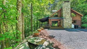 A cabin with a stone chimney, wooden exterior, and a porch with potted plants. - A peaceful retreat with a melody all it's own...come experience Maggie's Song! (Maggie Valley)