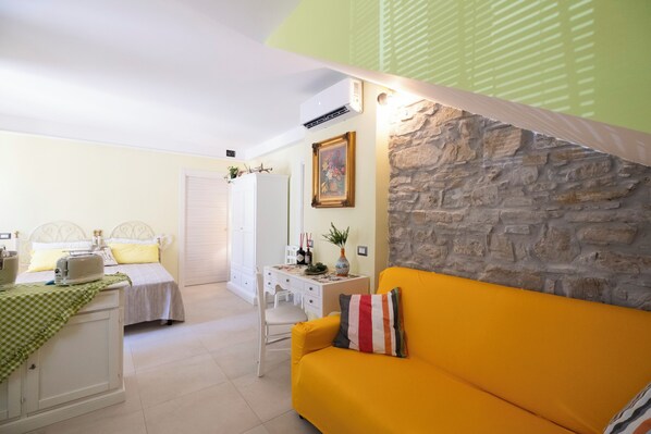 Una habitación con una cama, un sofá amarillo, un escritorio con una silla y una pared de piedra.