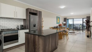 A modern kitchen with a central island, built-in appliances, and a dining area with a view. - 2 Bedroom In the Heart of Century City | Pool (Cape Town)