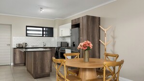 A modern kitchen with a central island, wooden chairs, and a vase with flowers. - 2 Bedroom In the Heart of Century City | Pool (Cape Town)