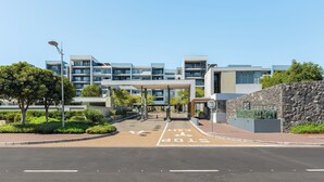 A modern building with multiple floors, a stone wall, and a clear sky. - 2 Bedroom In the Heart of Century City | Pool (Cape Town)