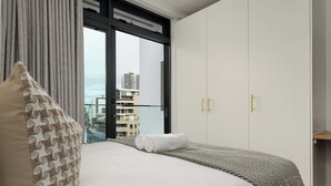 Une chambre d’hôtel avec un grand lit, une vue sur la ville par la fenêtre et une armoire dont les poignées sont dorées.