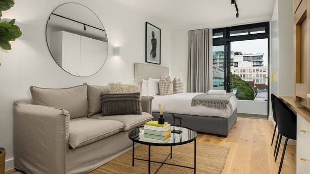 Une chambre d’hôtel moderne équipée d’un canapé, d’un lit, d’une table basse ronde et d’une grande fenêtre donnant sur la ville.