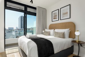 Relax in comfort with a large bed and city view, accompanied by a stylish table and artwork.