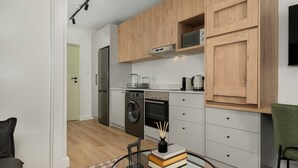 A modern kitchen with wooden cabinets, a built-in oven, and a washing machine. - The Sage l Studio l Luxury Finishes and Balcony View (Cape Town)